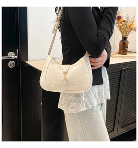 Close-up of cream glossy patent leather crescent shoulder bag with golden piston clasp