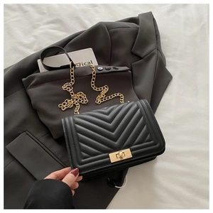 Detail of black V-quilted leather bag with golden rectangular turn-lock and chain strap