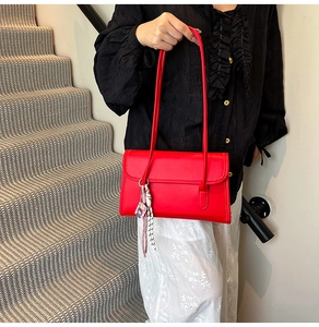 Detail of red matte leather underarm bag with decorative charm on indoor stairs