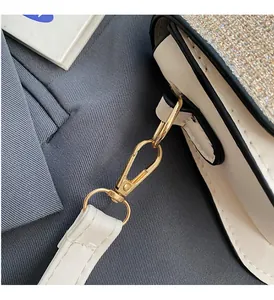 Close-up of a white leather crossbody bag with shimmering sequins and gold metal buckle