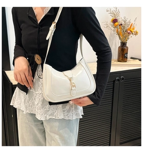 Detail of white patent leather hobo bag with a gold metal buckle and adjustable strap