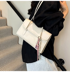 Detail of cream white shoulder bag with stylish rectangular flap and decorative charm