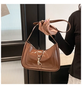 Close-up of brown glossy crescent saddle bag featuring a shiny gold metallic buckle closure