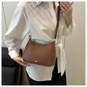 Détail d'un sac bandoulière en cuir marron avec logo en métal doré et sangle réglable