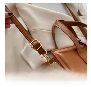 Close-up of brown leather bag featuring adjustable strap and bright gold metal hooks