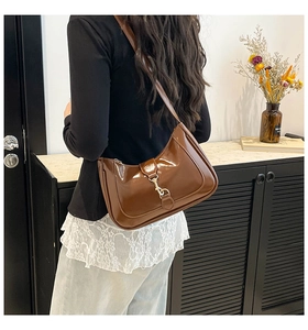 Brown patent leather hobo bag with gold metal buckle detail shown on shoulder