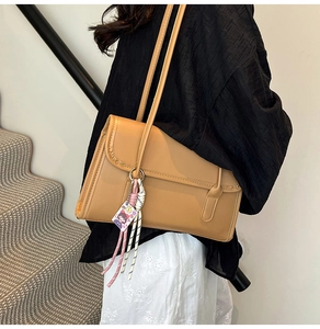 Side view of camel PU leather shoulder bag with buckle and woven pendant on model