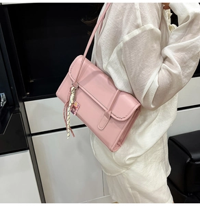 Detail showing pink leather shoulder bag with decorative cartoon tag and white woven rope