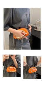 Detail view of orange patent leather handbag with oversized gold circular metal handle