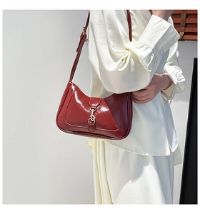 Model wearing a wine red patent leather baguette bag with a gold buckle clasp