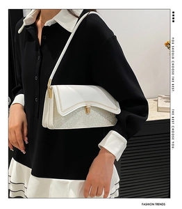 Detail of white leather shoulder bag with golden lock and silver glitter base detail