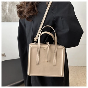 Detailed view of beige square tote bag with knot charm worn on a black long coat
