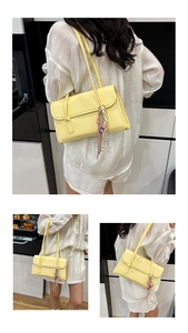 Detail view of pale yellow minimalist shoulder bag with fine stitching and ribbon charm