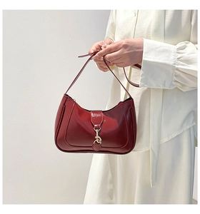 Detail of burgundy patent leather saddle bag with glossy finish and gold metal hook