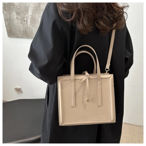 Detail view of beige crossbody bag with double handles and elegant gold-tipped knot decor