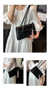 Detail of black matte leather tote bag featuring a pink woven tassel and slim straps