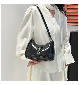 Detail of black patent leather hobo bag with gold metal buckle on a shoulder strap