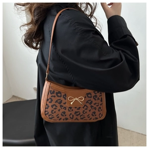 Sac sous le bras marron avec motif léopard et boucle nœud doré porté par un mannequin