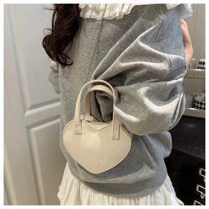 Détail d'un mini sac cœur en cuir crème avec bandoulière chaîne et doubles poignées