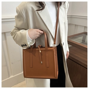 Brown rectangular crossbody bag with minimalist knot detail worn by a model in a beige suit