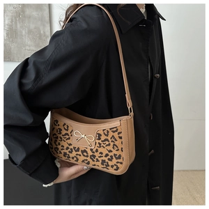 Model wearing leopard print underarm bag with golden bow clasp over black coat