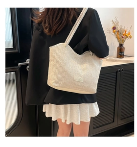 Élégant grand sac fourre-tout en paille tressée beige porté par un mannequin.