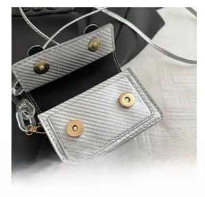 Detail of silver square bag featuring carbon fiber texture and golden magnetic snaps
