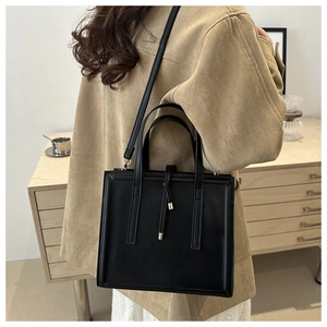 Detail view of the black leather vertical crossbody bag with side tassel and gold hardware