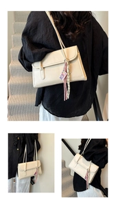 Detail of cream underarm bag with double slim straps and colorful woven pendant