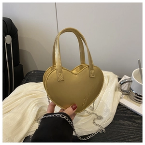 Détail d'un sac à main doré en forme de cœur avec texte gaufré et chaîne en métal argenté
