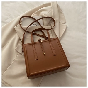 Detailed close-up of brown textured leather tote bag with gold metallic pendant detail