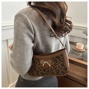 Détail du sac léopard sous le bras avec nœud doré et bordures en cuir marron chic