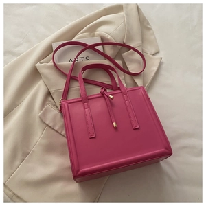 Detailed view of magenta crossbody bag with tassel and gold hardware on beige suit