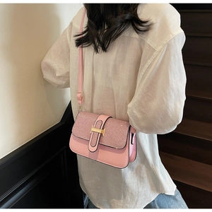 Detail of pink glitter flap shoulder bag with gold H-buckle worn by a model in casual outfit