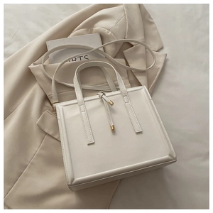 Flat lay of cream leather vertical tote bag with gold hardware on blazer background