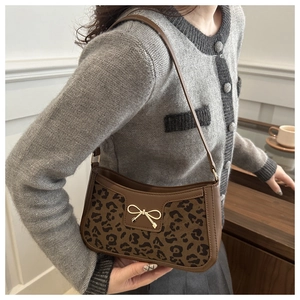 Detail of leopard print fabric and gold bow buckle on a brown leather baguette bag