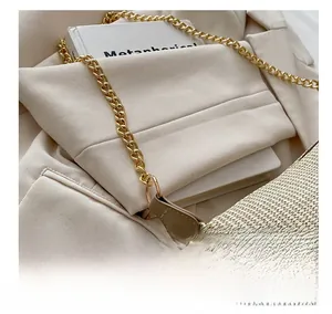 Détail d'un sac tissé beige clair avec bandoulière chaîne dorée sur un blazer