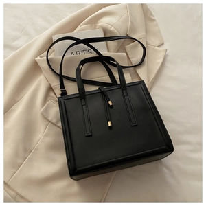 Close-up of black structured tote bag with gold hardware and tassel detail on a beige blazer