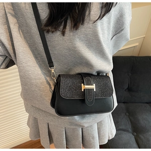 Detail showing the black crossbody bag with sequin flap and golden H buckle on a model