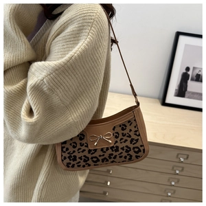 Detail of leopard print underarm bag with gold bow clasp worn over a beige sweater