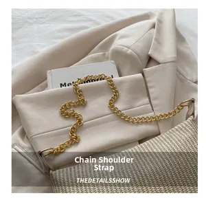 Détail du sac tressé avec bandoulière chaîne dorée sur fond de tissu beige doux