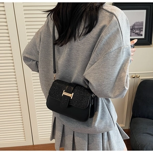Detail of black crossbody bag with shimmering flap and golden H-shaped metal clasp buckle
