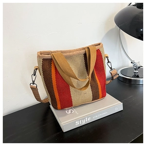 Détail du sac fourre-tout en maille rayée avec bandoulière posé sur un livre