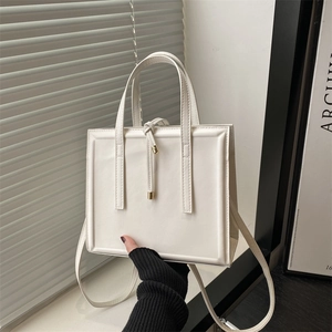 Minimalist white leather tote bag with gold accents and shoulder strap for elegant commuting