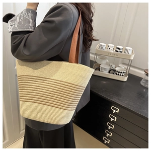 Detail of striped straw tote bag with reinforced brown woven shoulder straps