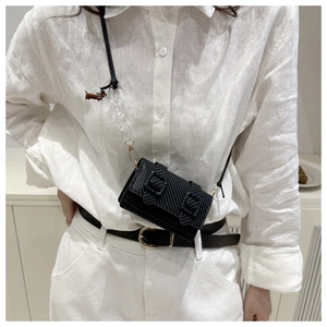 Mini black crossbody bag detail with brown puppy charm and acrylic chain on white outfit
