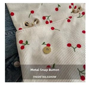 Détail du tissu en velours côtelé à motif cerise avec fermoir magnétique doré sur un sac