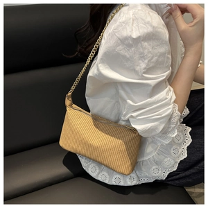 Détail du sac à main tissé kaki avec chaîne métallique porté sur chemise dentelle