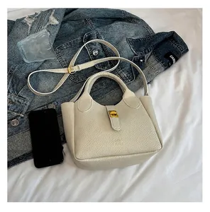 Detail view of a white pebbled leather bucket bag with gold lock in lifestyle setting