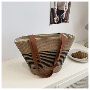 Detail of woven straw tote bag with black stripes and brown handles in home setting